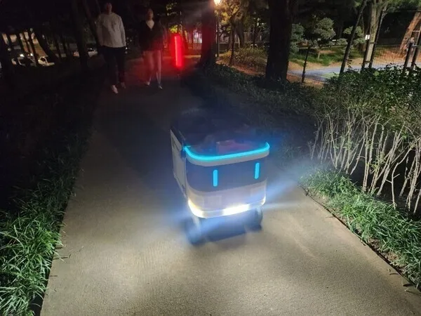 밤길을 따라 파란 빛을 발하며 자율주행하는 작은 배달 로봇.